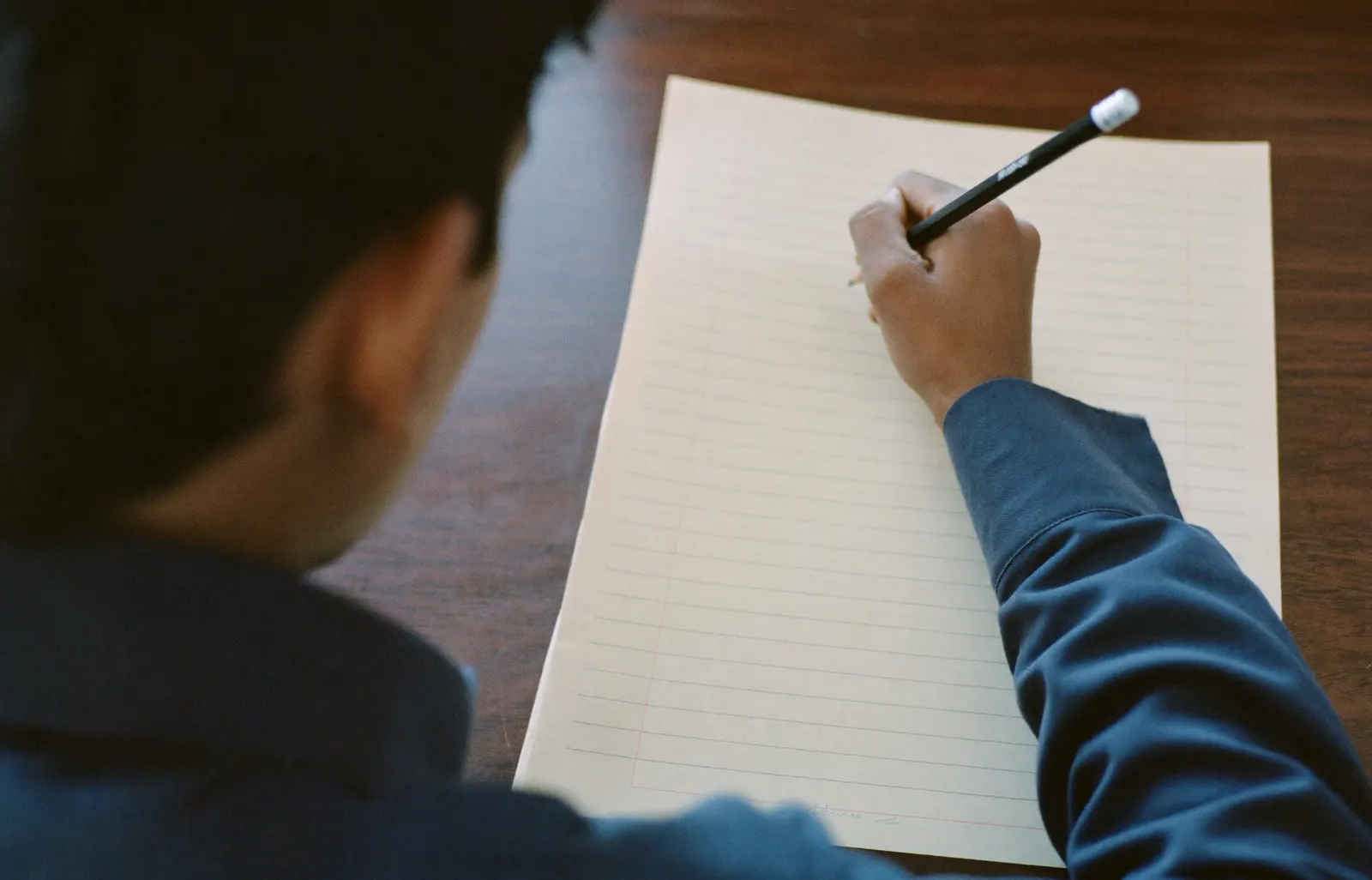 A student writing at a wooden desk